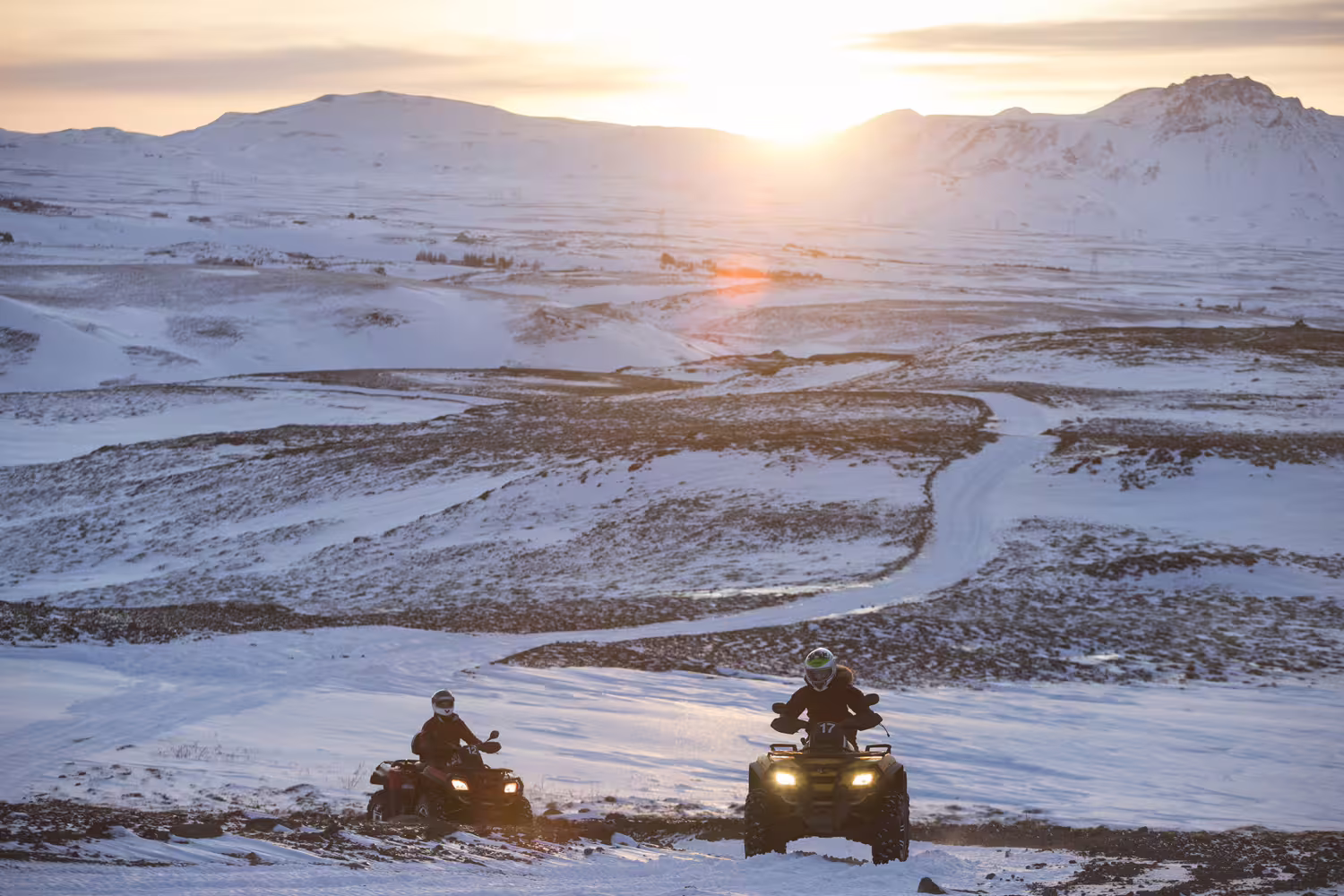 ATV riders explore snowy landscapes during the Reykjavik Peak 1-hour tour, set against a stunning Icelandic winter sunset.