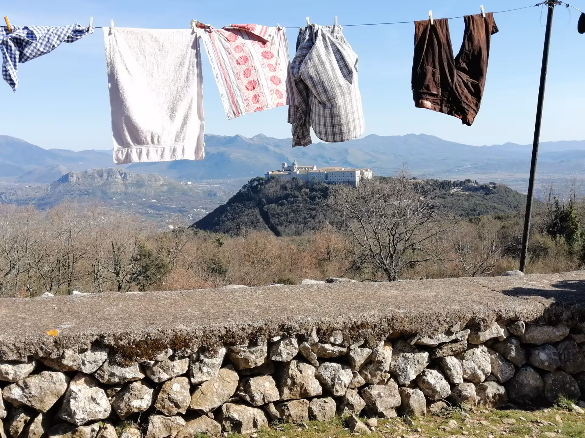 A clothesline with colorful laundry frames a scenic view of the historic hilltop monastery at L'Anello della Collina Imprendibile.