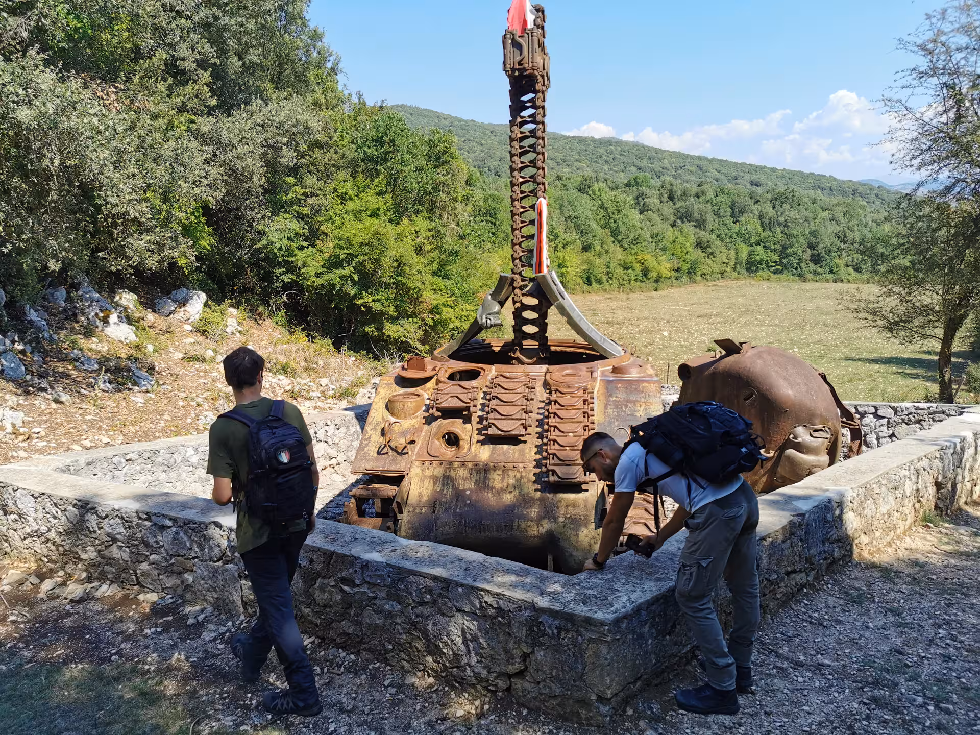 Two tourists exploring a rusted tank relic on the L'Anello della Collina Imprendibile tour.
