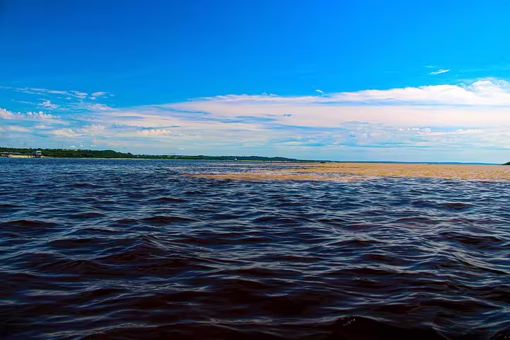 Vibrant meeting of Rio Negro and Amazon River waters under a clear blue sky on the Amazon Jungle Adventure tour.