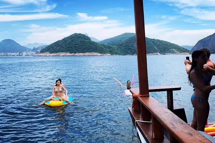 Tourists relaxing and taking photos from a boat with stunning views of Rio's coastal landscapes.