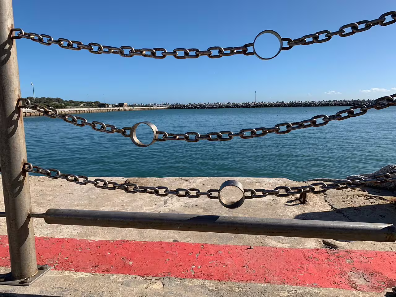 View of the ocean from the Robben Island dock, framed by metal chains and clear blue skies.