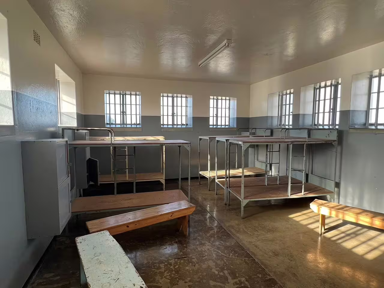 Robben Island prison dormitory with multiple metal bunk beds and benches, reflecting South Africa's historical heritage.