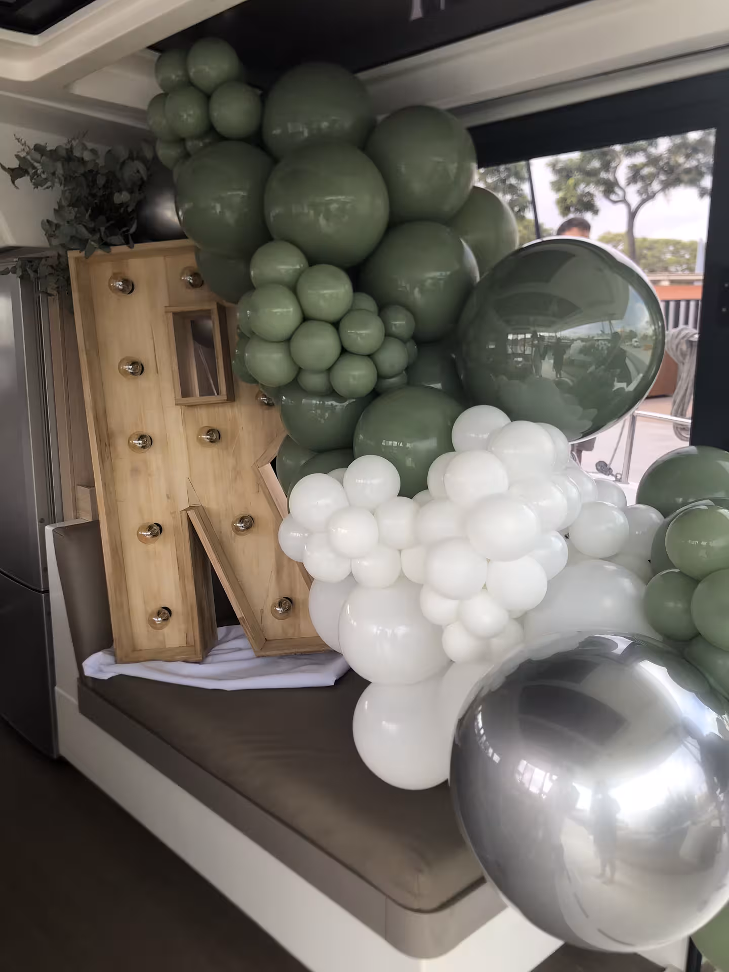 Romantic yacht proposal decor with green and white balloon arch and lighted letter N backdrop onboard