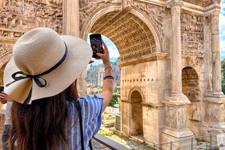 Tourist capturing the Arch of Constantine in Rome, ideal for a cultural tour with pizza and gelato class.
