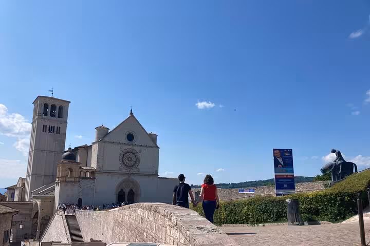 Visitors walking towards the Basilica of Saint Francis in Assisi under a clear blue sky during a private Rome day tour.