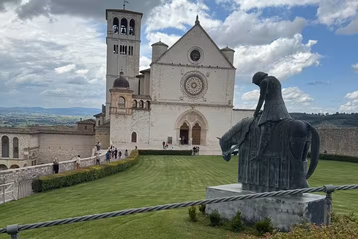 Statue of a knight and the Basilica of Saint Francis in Assisi with cloudy skies on a private day tour from Rome.