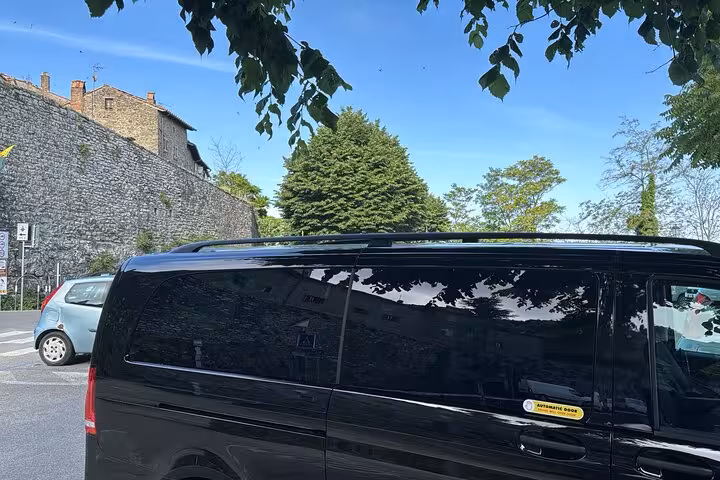 Black tour van in scenic Assisi street, offering comfortable travel experience from Rome.
