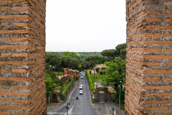 View from the Aurelian Walls over a tree-lined Roman road and city gates on a family friendly Rome walls walking tour