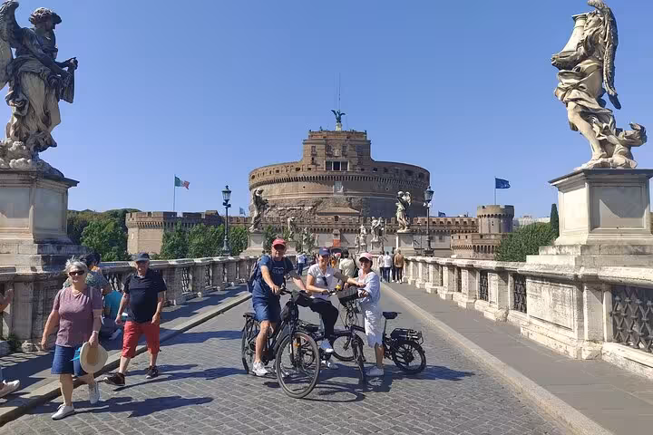 Cyclists enjoy a Rome E-Bike tour by Castel Sant'Angelo on a sunny day.