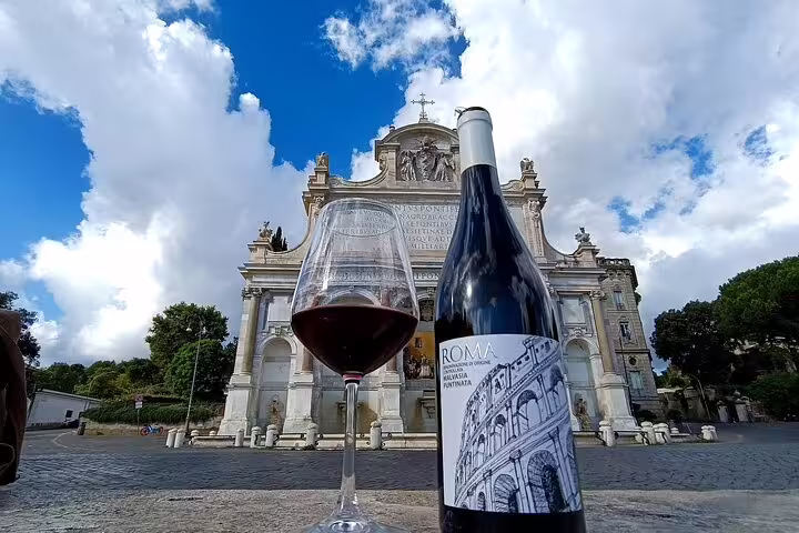 Glass of red wine and bottle labeled Roma in front of historic Roman church, highlighting Fabullus wine pairing experience