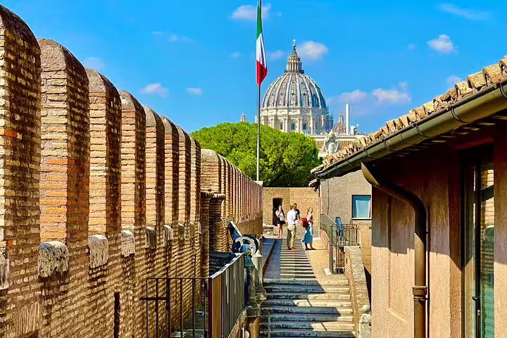 Guided Rome tour guests walk along Castel Sant’Angelo ramparts with views of St Peter’s Basilica dome and Italian flag