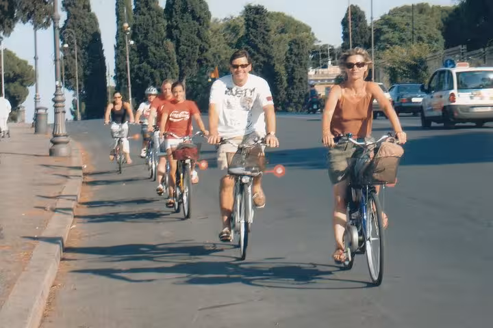 Cyclists ride e-bikes along a scenic road in Rome, part of a small group tour exploring the city's famous attractions.