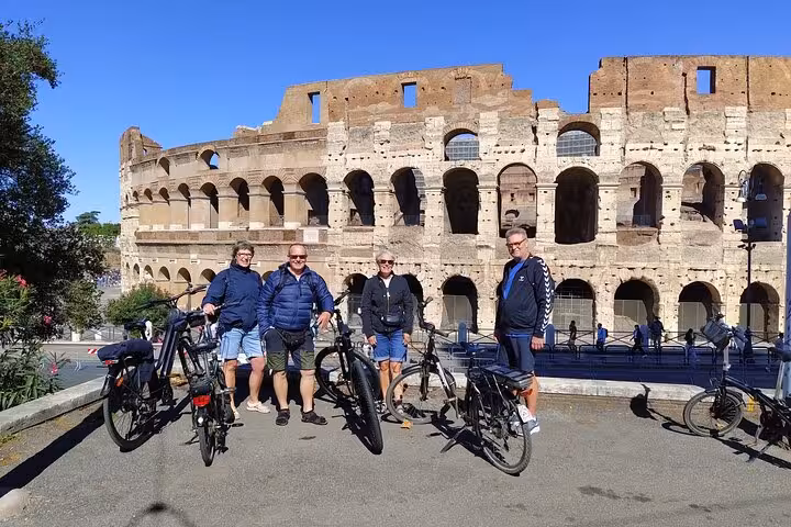 Visitors pause with e-bikes at the Colosseum during the Rome Highlights E-Bicycle tour, enjoying ancient Roman architecture.