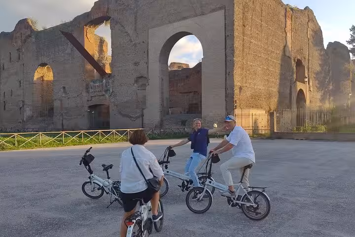 Tourists on e-bikes admire ancient ruins in Rome, offering a unique small group experience of historic landmarks.