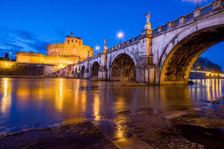 Illuminated Castel Sant’Angelo and Ponte Sant’Angelo reflected on the Tiber River during a private Rome by night chauffeur tour