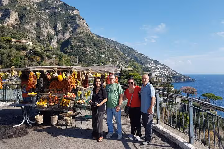 Travelers at a roadside fruit stand with panoramic Amalfi Coast views on a day trip from Rome