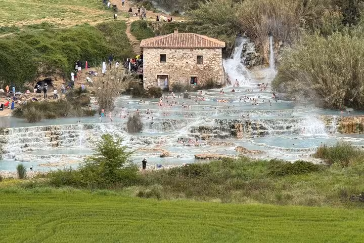 Tourists enjoying the natural thermal pools at Terme di Saturnia, surrounded by lush greenery and a rustic stone building.
