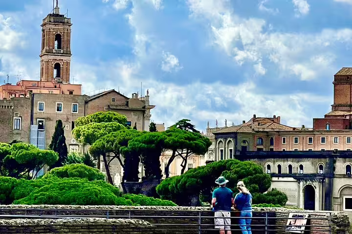 Visitors on a guided Rome Trajan Markets tour overlooking the Imperial Forum ruins and historic skyline with medieval bell tower