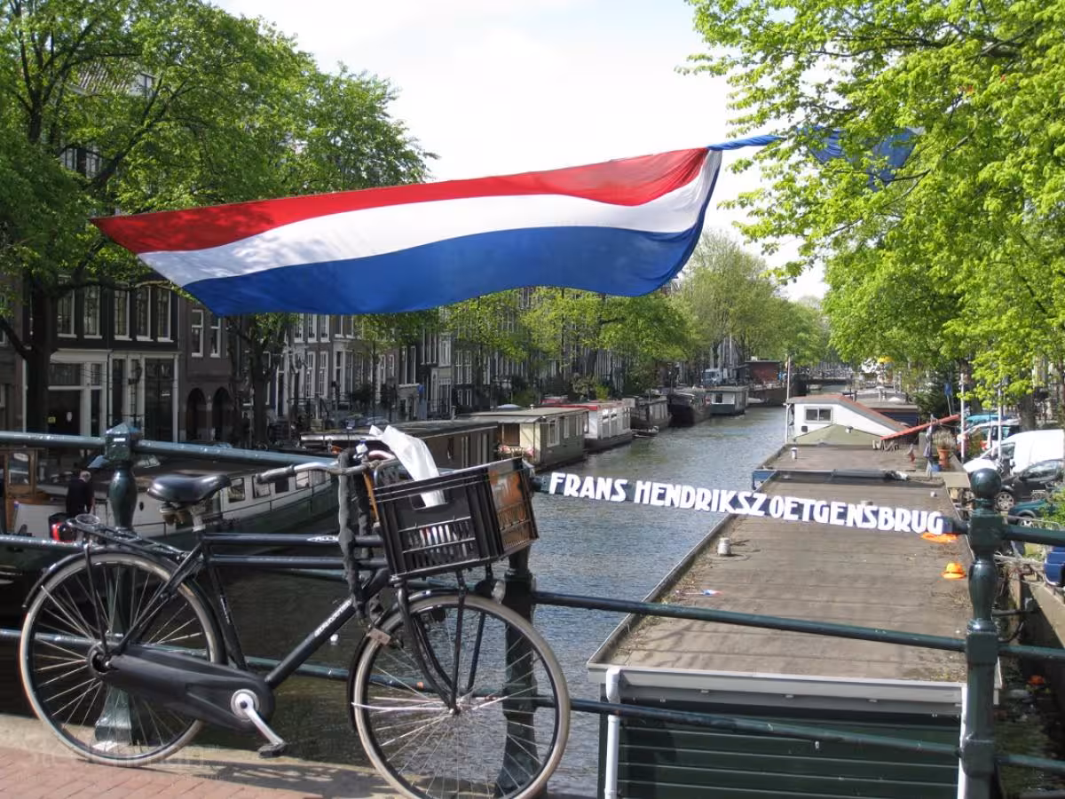 Amsterdam canal bridge with Dutch flag and bicycle, featured on private tour from Rotterdam to Kinderdijk