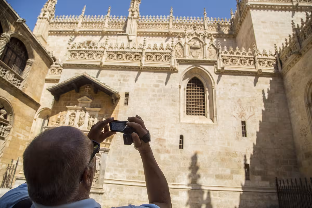 Tourist capturing the ornate Gothic facade of the Royal Chapel under a clear blue sky during guided tour.