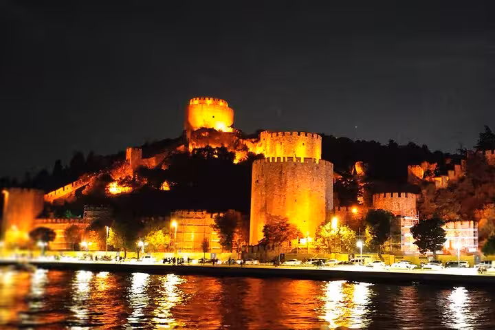 Rumeli Fortress illuminated at night seen from Istanbul Bosphorus dinner cruise, waterfront lights reflecting on water