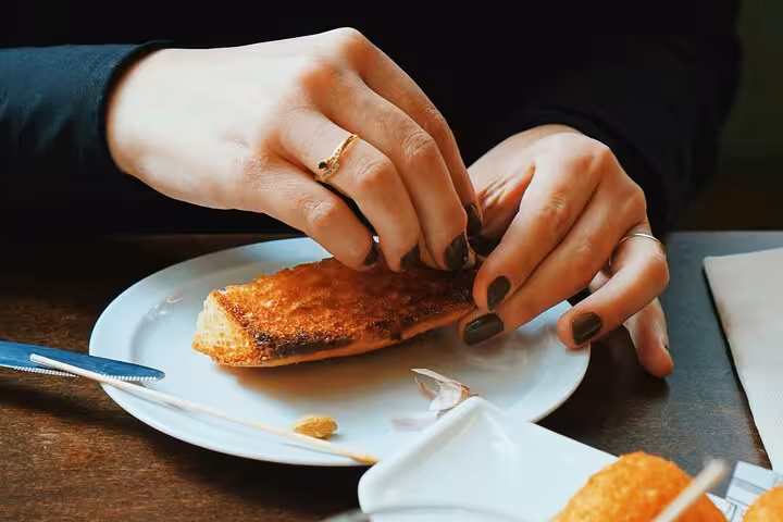 Hands sharing crispy tapa at a local Ruzafa bar, part of the evening food and wine tour with drinks