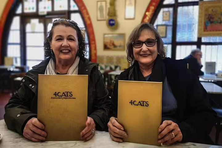Two smiling women holding menus at 4 Gats, a historic café in Barcelona, before their Sagrada Familia and Gaudi tour.