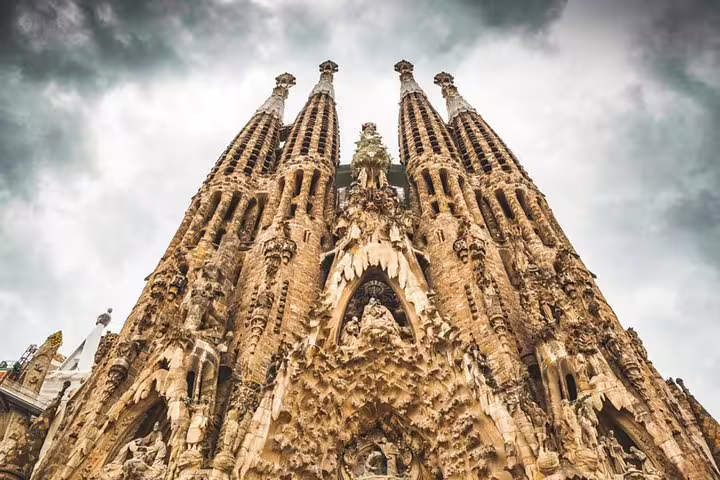 Majestic view of Sagrada Familia's intricate facade under dramatic skies, featured in a Gaudi tour with skip-the-line access.