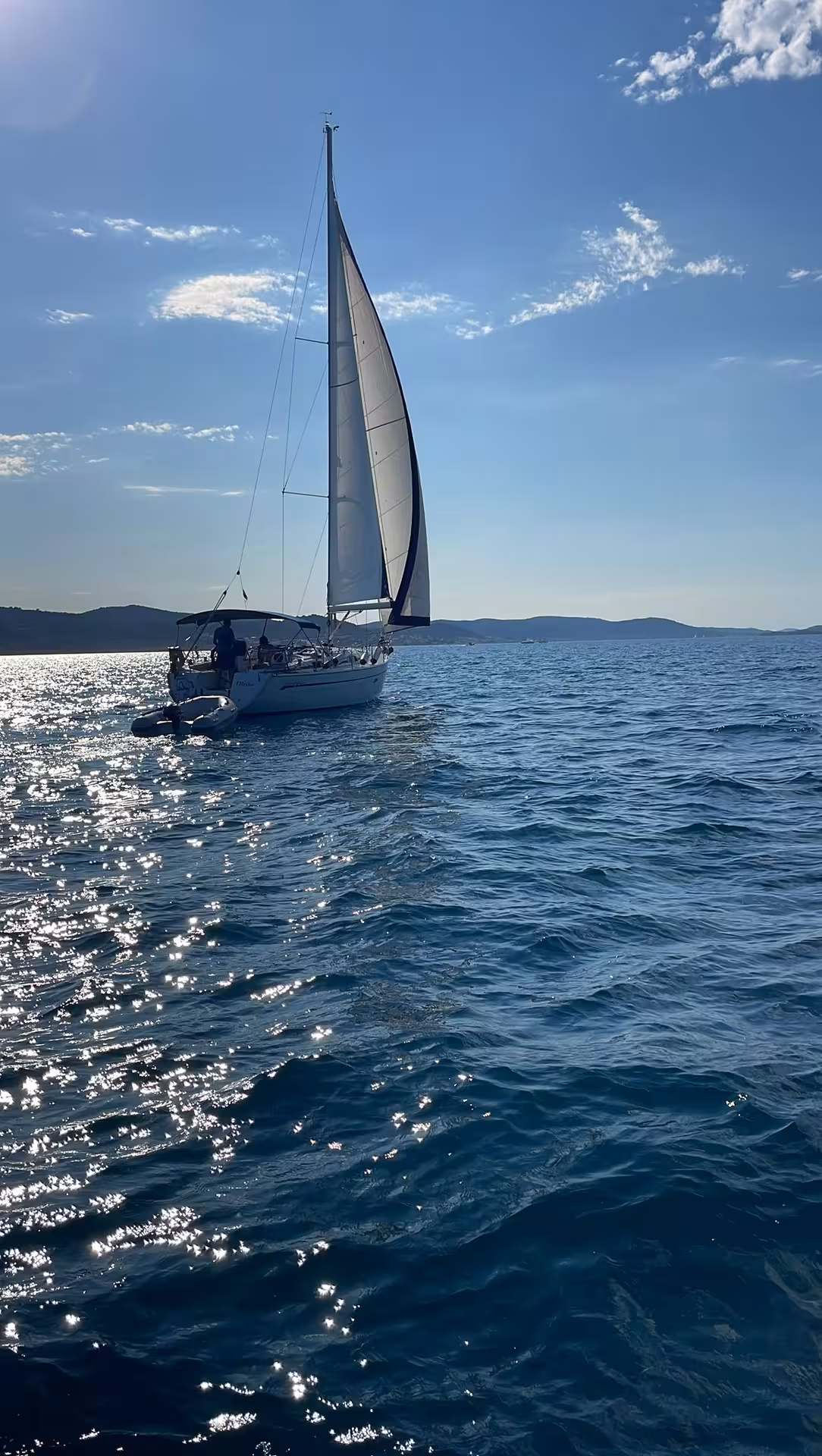 Sailboat gliding at sunset on calm open water, scenic Sailing Adventure cruise with coastal views