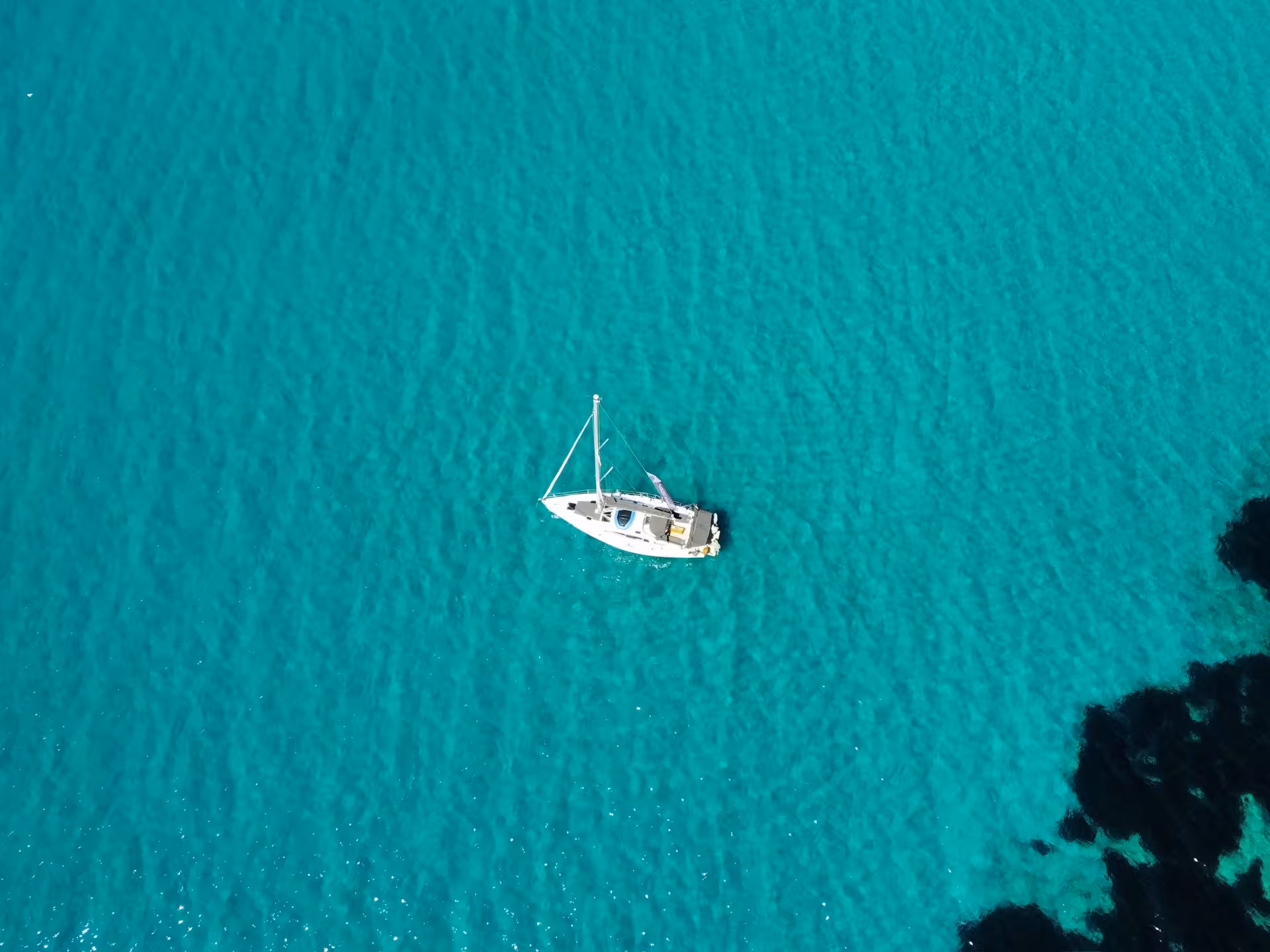 Top-down view of a sailboat on vibrant turquoise water near reefs, showcasing a relaxing Sailing Adventure cruise