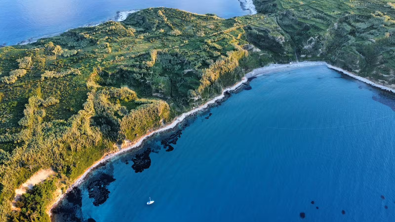 Panoramic aerial of quiet island coastline and blue lagoon with sailboat, ideal route for a sailing adventure trip