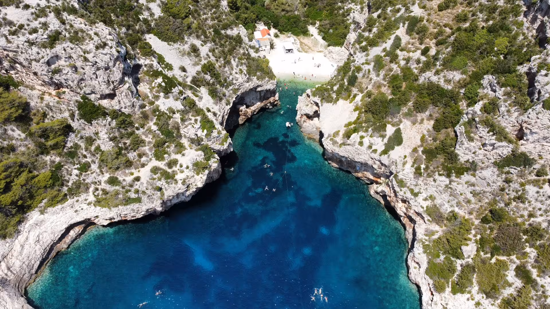 Drone view of rocky sea cove with crystal-clear water and swimmers, perfect stop on a sailing adventure cruise
