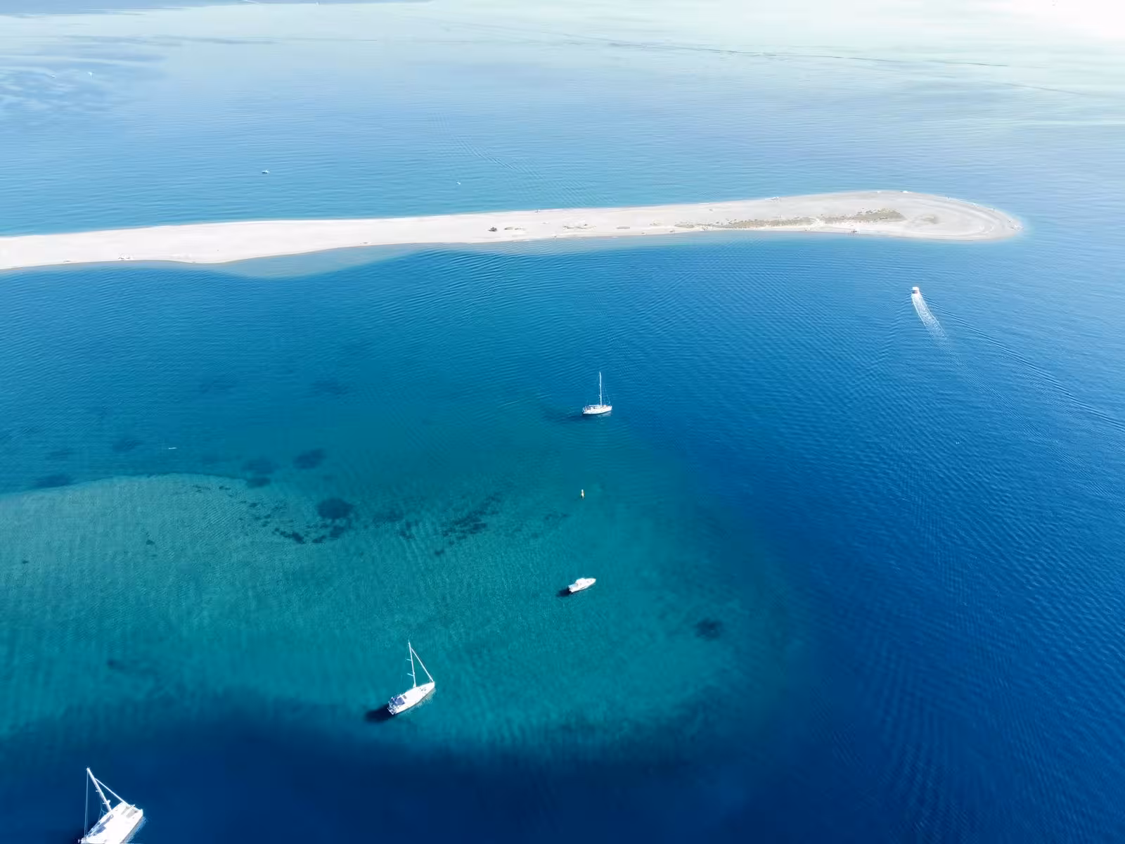 Drone shot of sandbar and anchored sailboats in crystal-clear blue sea, ideal for a Sailing Adventure day trip
