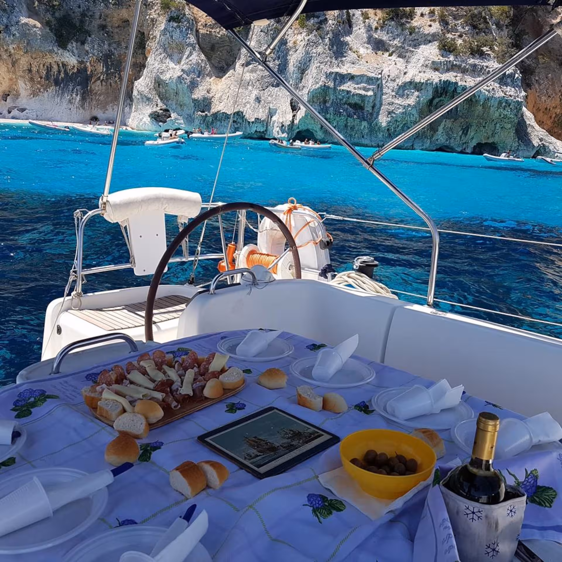 Gourmet lunch setup on a sailing boat with stunning views of the Gulf of Orosei's turquoise waters and cliffs.