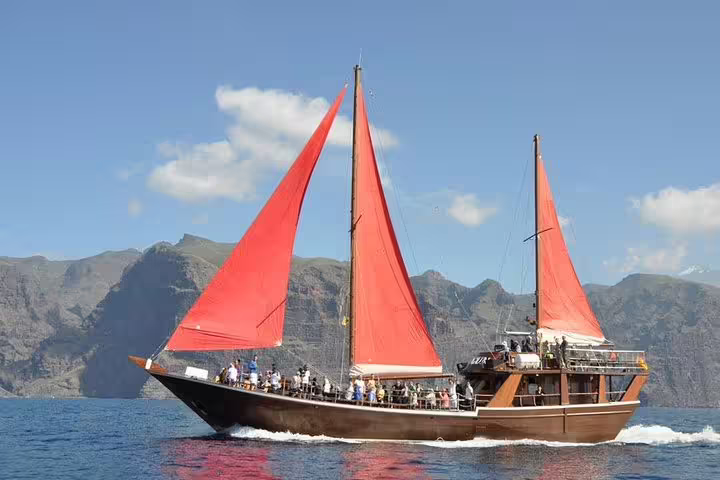 Sailing boat with red sails gliding near Los Gigantes, perfect for whale and dolphin watching tours.
