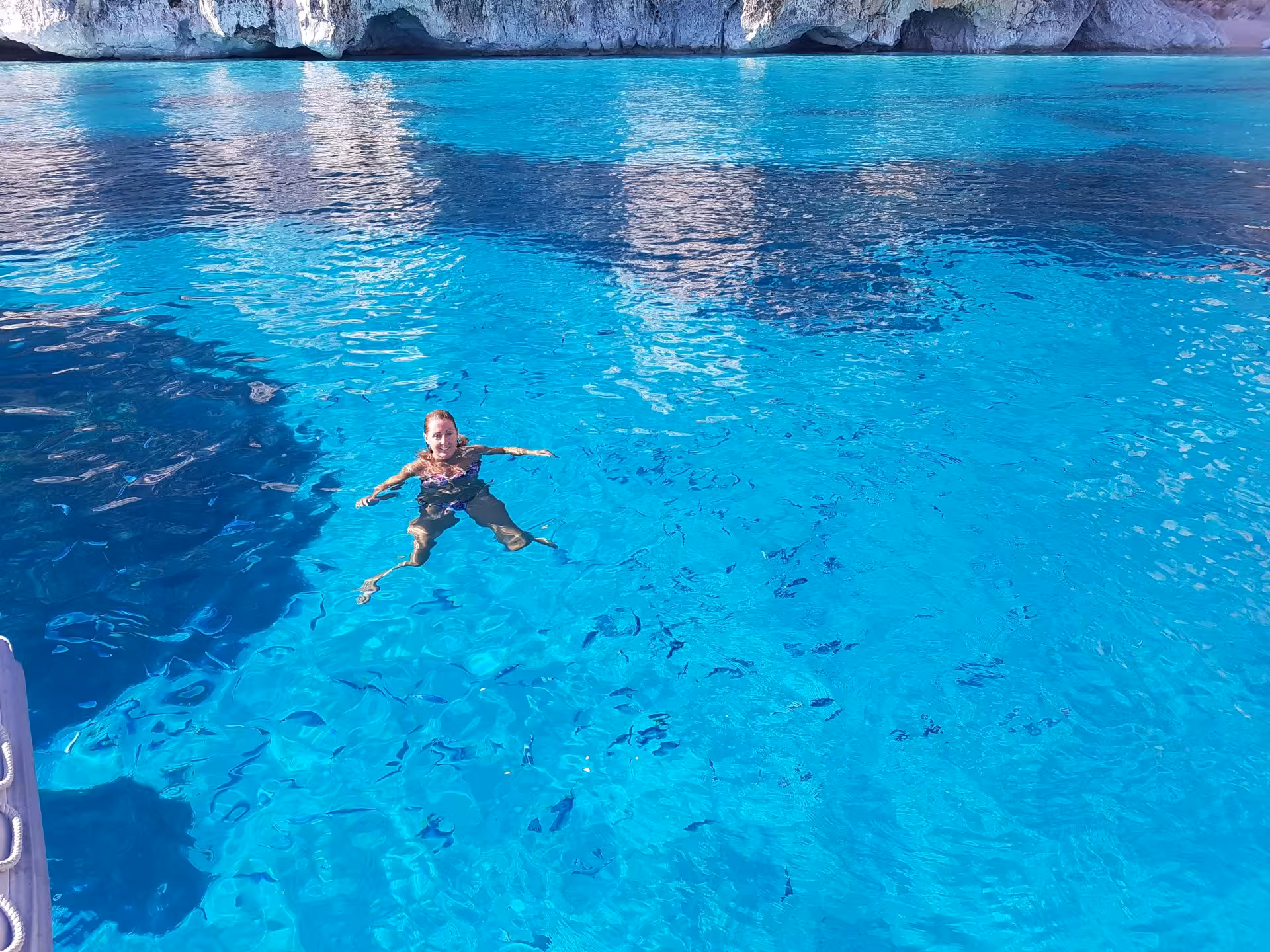 A person swimming in crystal-clear turquoise waters near rocky cliffs in the Gulf of Orosei, Sardinia.