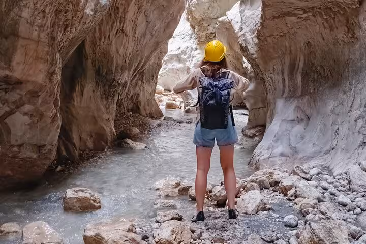 Adventurer exploring the narrow, rocky passage of Saklıkent Canyon with a safety helmet and backpack.