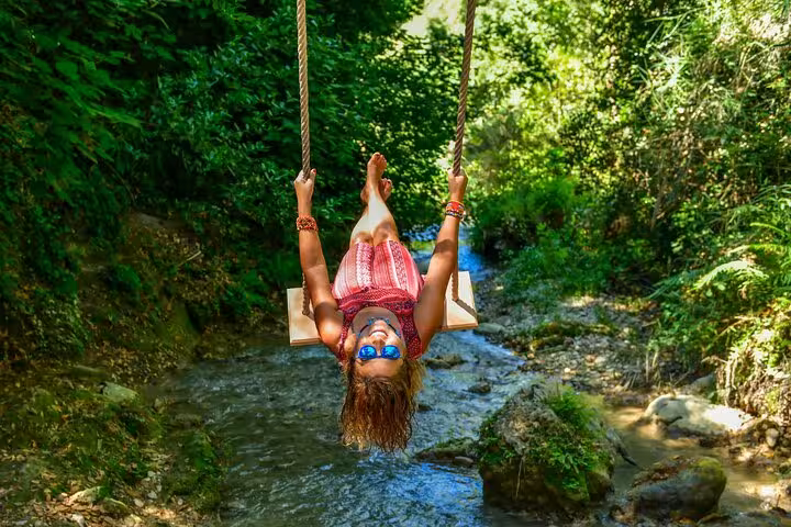 Tourist enjoying a swing over a serene creek surrounded by lush greenery in Saklıkent Canyon near Fethiye.