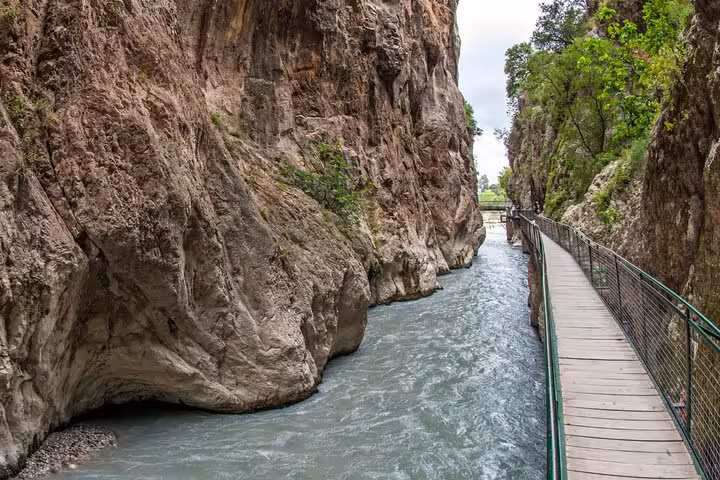 Narrow path along the rushing waters of Saklıkent Canyon, showcasing dramatic rock formations and lush greenery.