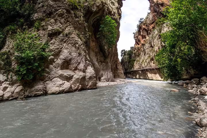 Scenic view of Saklıkent Canyon's rushing river, flanked by towering rocky cliffs and vibrant foliage.