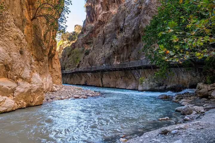 River flowing through the majestic Saklıkent Canyon with a scenic wooden walkway alongside rocky cliffs.