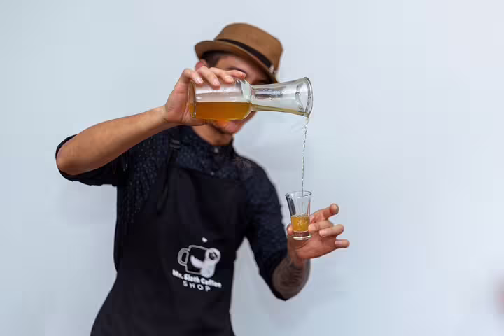Man in hat pours craft cocktail during San Jose night tour, highlighting mixology experience at farm-to-table event.