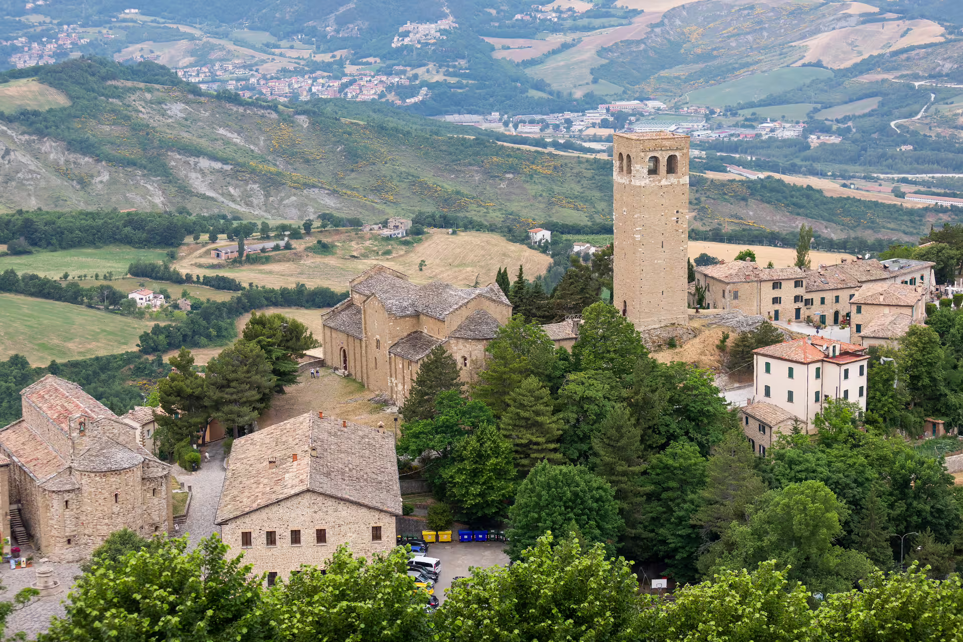 Panoramic view of San Leo village with historic fortress and tower amidst lush green hills.