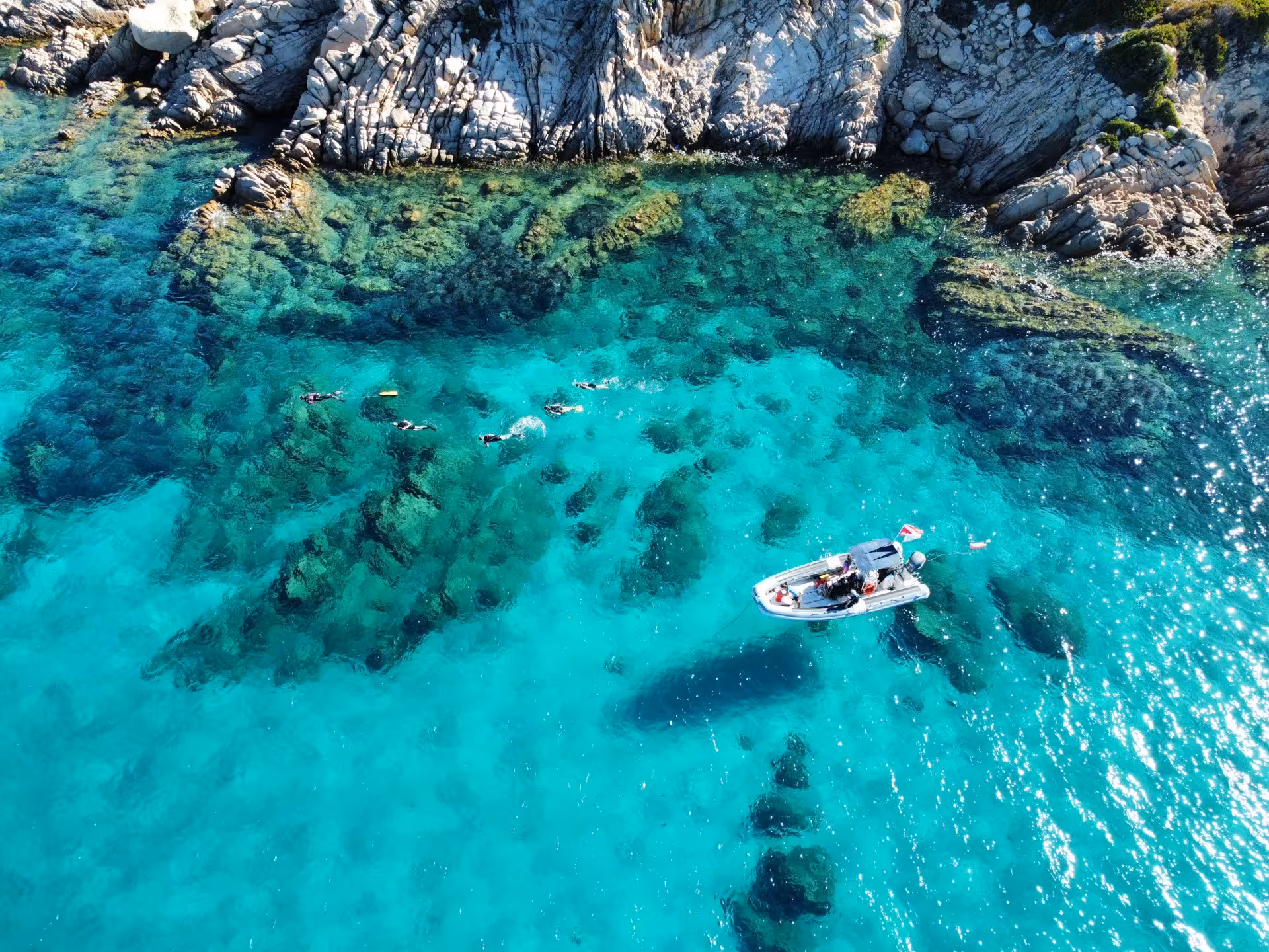 Pristine turquoise waters with snorkelers and a boat near the rocky shores of Molara Island in San Teodoro.