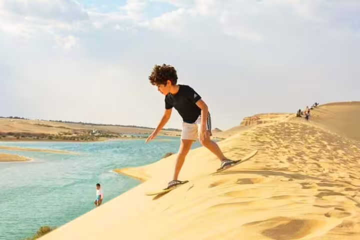 Sandboarding on golden dunes by a blue lake in El Fayoum Oasis, Egypt, on an overnight camping tour from Cairo