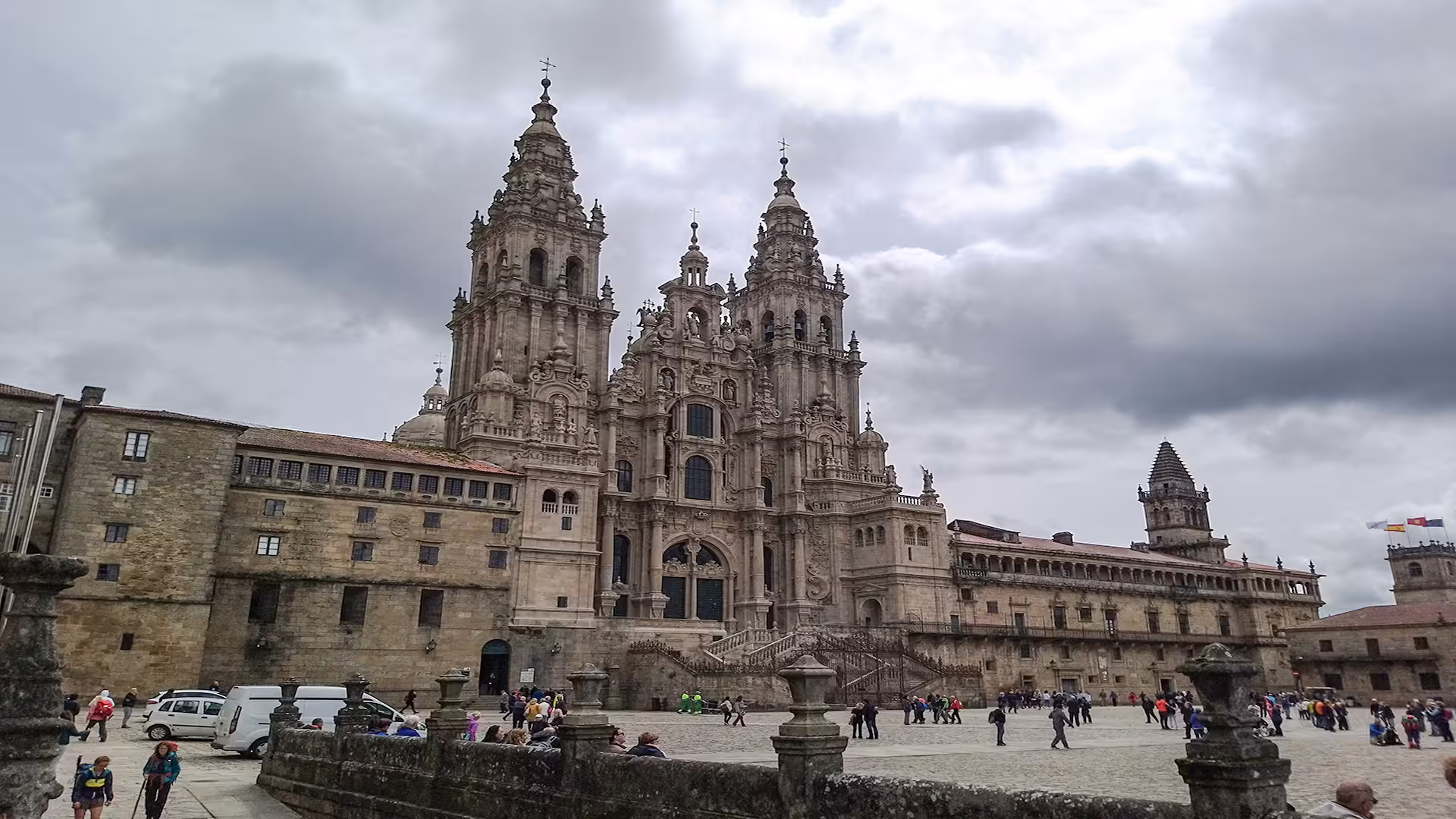 Tourists explore the grand Santiago de Compostela Cathedral under a dramatic sky, highlighting its architectural magnificence.
