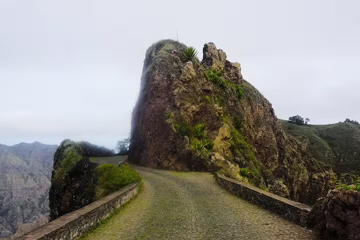Narrow cobblestone path winds around a dramatic rocky outcrop on Santo Antão's scenic island tour.