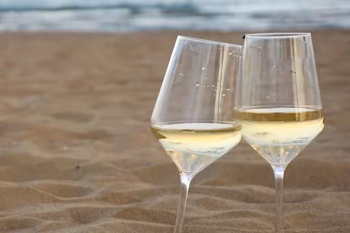 Two glasses of Santorini Assyrtiko white wine on a sandy beach, local tasting add-on for private SUV tour