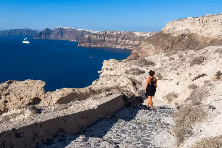 Traveler walking Santorini caldera cliff path with Aegean sea views during Explore Santorini with your 5-Senses tour